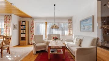 A living room with a wooden ceiling, a sofa set, a coffee table, a bookshelf, and a painting on the wall.