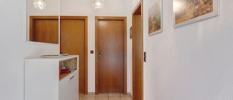 Een hal met een wit kastje, een rode vloerkleed, houten deuren en twee hanglampen.