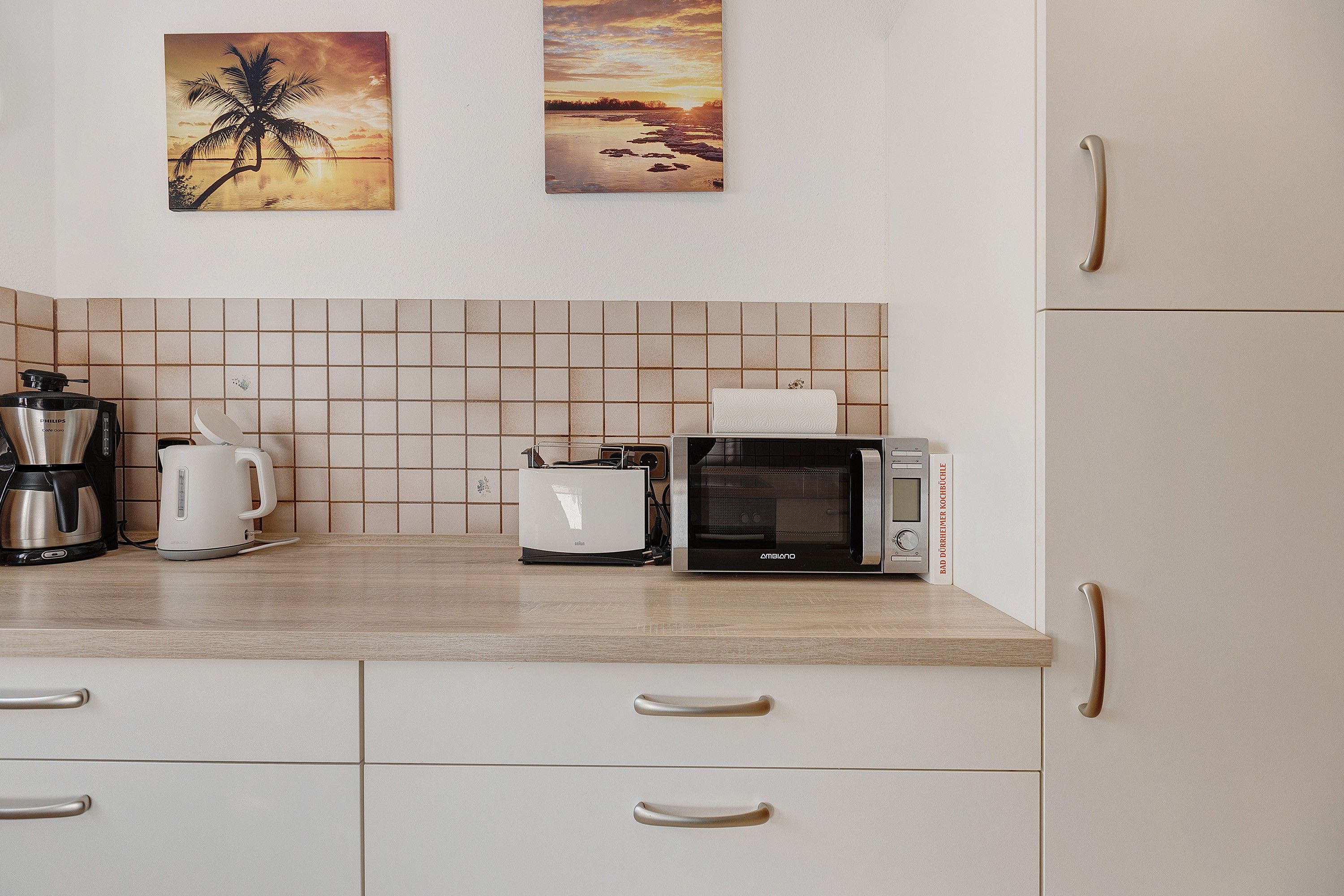 Eine Küche mit gefliestem Rückspritzschutz, einer Kaffeemaschine, einem Toaster, einer Mikrowelle und einem Schrank mit Schubladen.