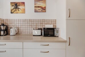 Eine Küche mit gefliestem Rückspritzschutz, einer Kaffeemaschine, einem Toaster, einer Mikrowelle und einem Schrank mit Schubladen.