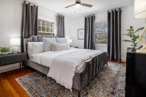 A bedroom with a bed, bedside tables, a floor lamp, a ceiling fan, and a window with curtains. - Luxe Dutch Colonial in The Heart of Laurelhurst (Portland)