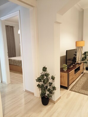 A modern living room with a wooden TV stand, a potted plant, and a lamp. - Marousi Residence with Green Garden (Marousi)