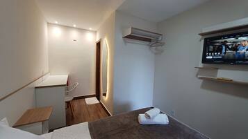 A modern hotel room with a wooden floor, a small table, a TV mounted on the wall, and a towel on the floor.