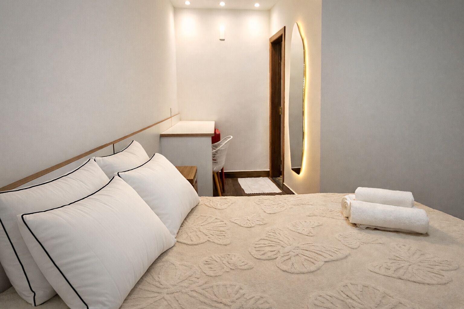 A hotel room with a bed, pillows, a bedside table, a mirror, and a towel.