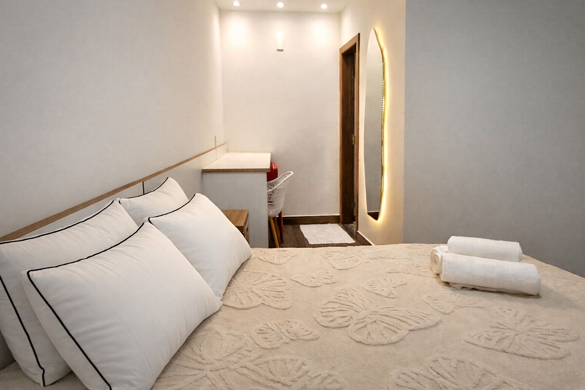 Una habitación de hotel con cama, almohadas, mesita de noche, espejo y toalla.