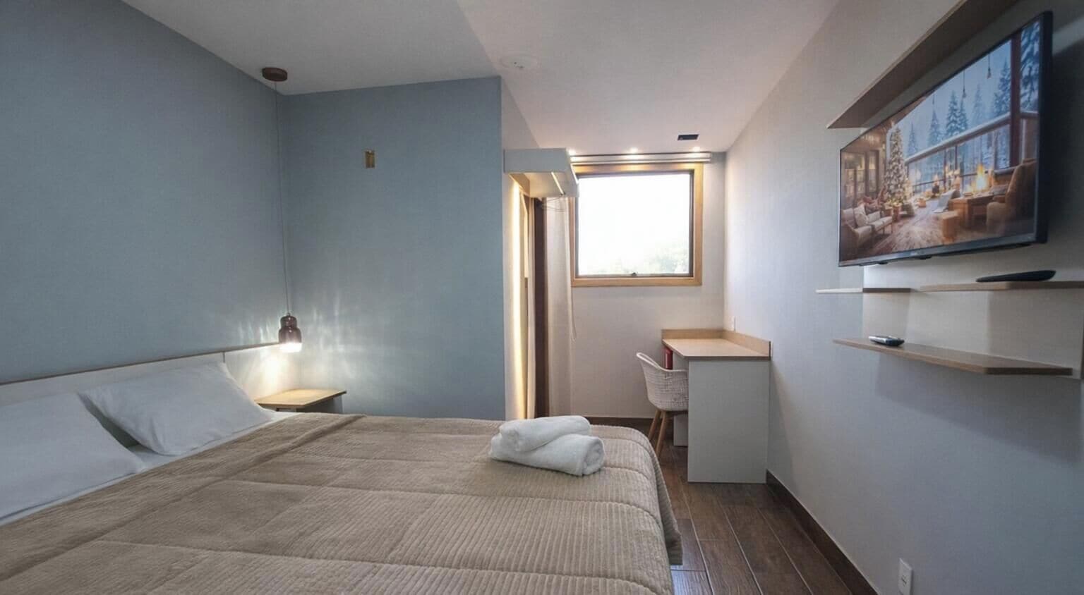 Un dormitorio con una cama, un escritorio, una silla, un ventanal y un televisor.