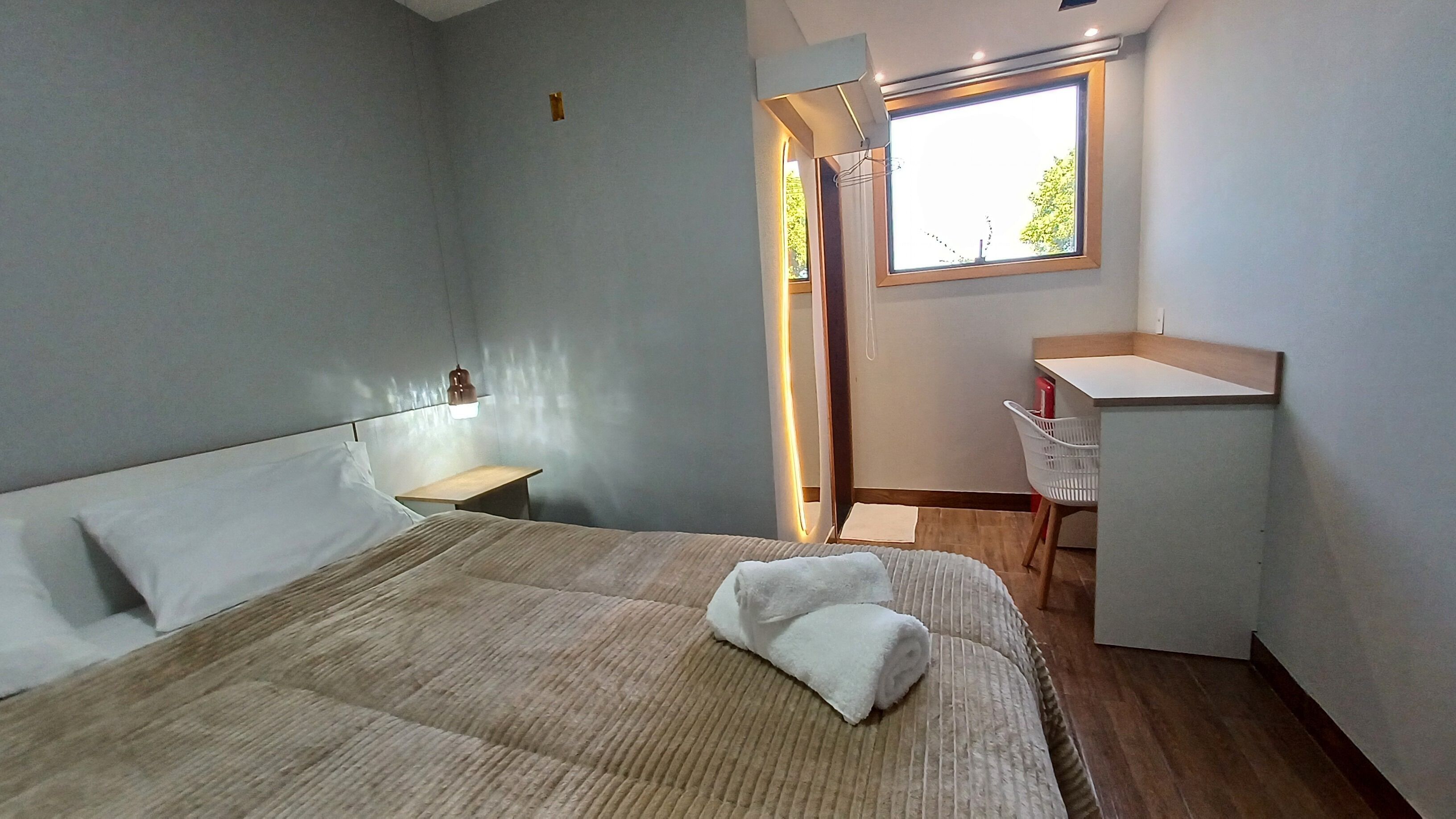Un dormitorio con cama, mesita de noche, escritorio, silla y ventana.