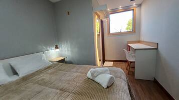 Un dormitorio con cama, mesita de noche, escritorio, silla y ventana.