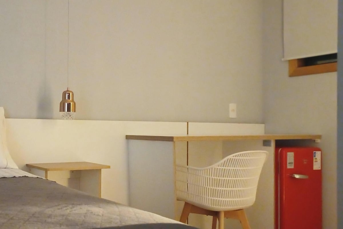 A hotel room with a bed, a desk, a chair, and a red refrigerator.