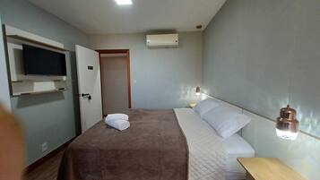 Quarto com cama, televisão fixada na parede, aparelho de ar condicionado e abajur.