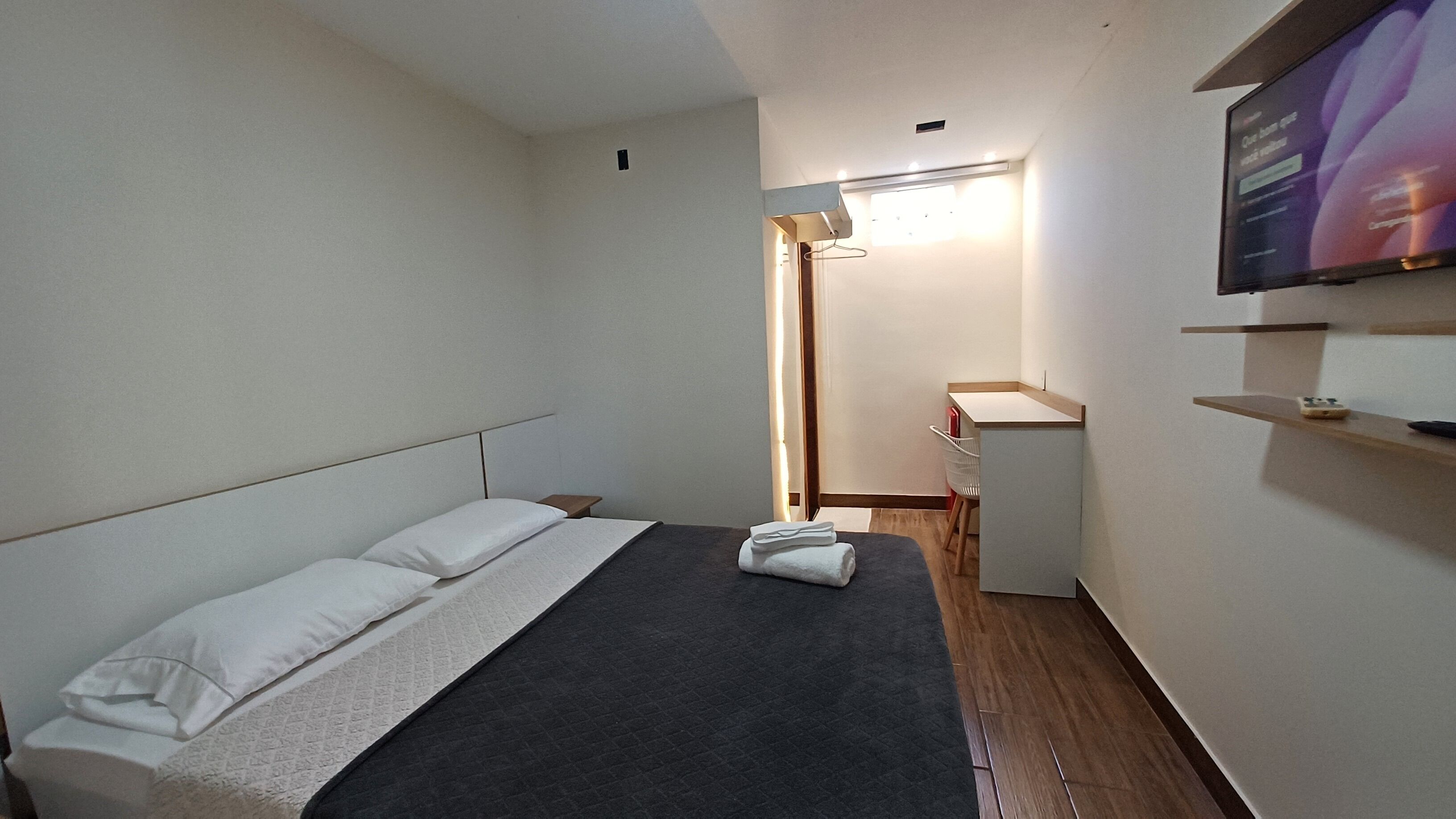 Camera d'albergo con un letto, una scrivania, una sedia, un televisore montato a parete e una finestra con tende.