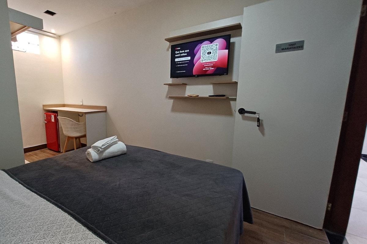 Una habitación de hotel con cama, un pequeño escritorio, televisión y una puerta con un cartel.