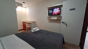 Una habitación de hotel con cama, un pequeño escritorio, televisión y una puerta con un cartel.
