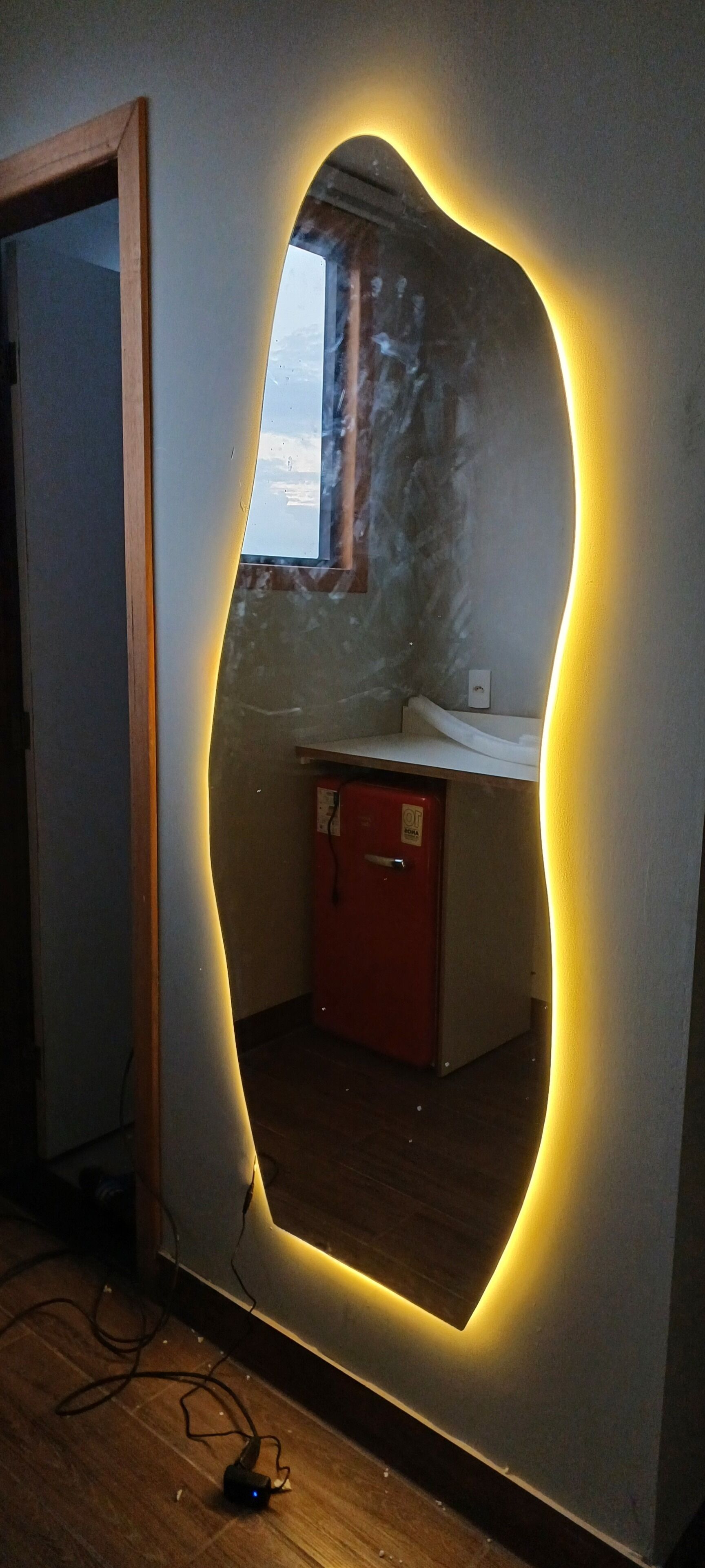 A room with a unique wall mirror, a red cabinet, and a visible window.