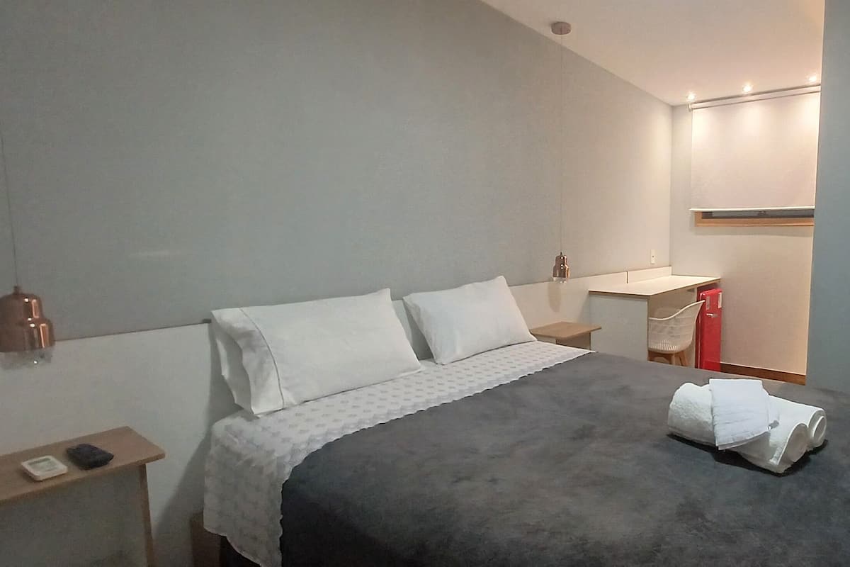 Una habitación de hotel con cama, mesita de noche y un pequeño escritorio con silla.