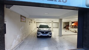 Um carro estacionado em um corredor com piso de azulejos, paredes brancas e uma escada ao fundo.