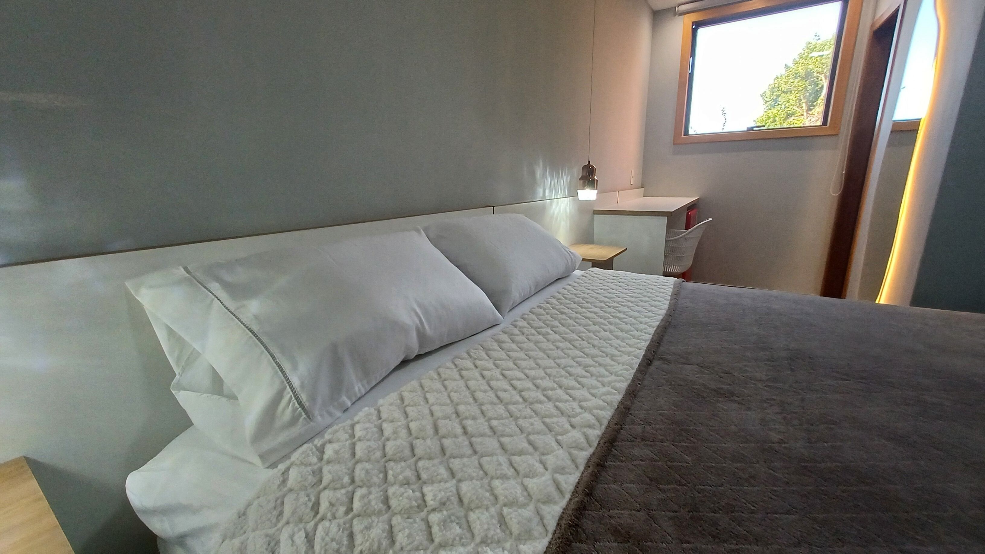 A bedroom with a bed, a nightstand, a desk, and a window.
