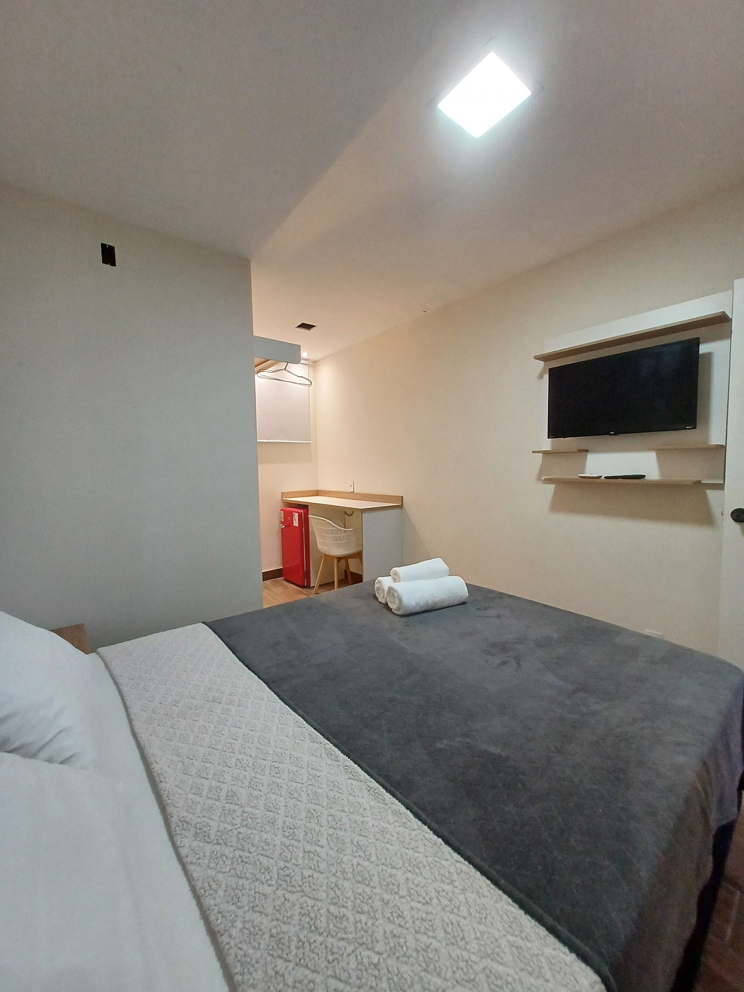 Habitación de hotel con cama, televisor de pantalla plana en la pared, escritorio con silla y refrigerador rojo.