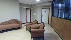 Uma área de espera com três sofás, piso ladrilhado e uma porta com a inscrição 'Sala de Espera'.