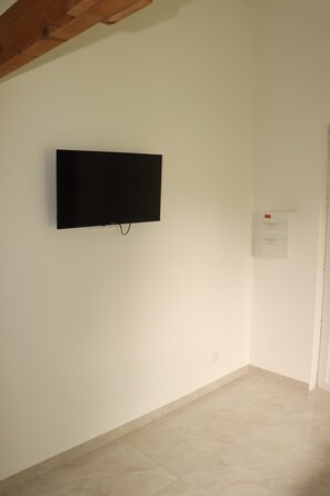 Une pièce avec un téléviseur fixé au mur, une porte et un sol carrelé.