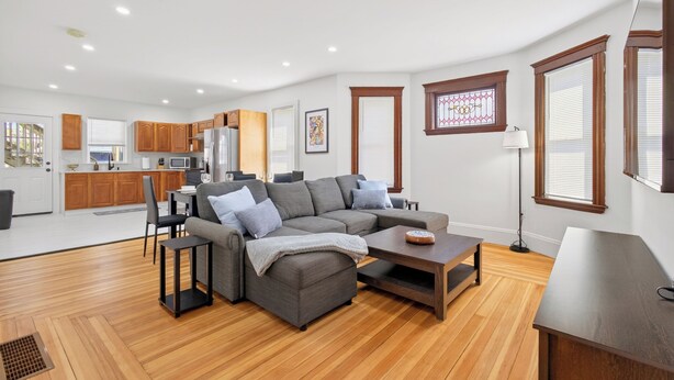 Uma sala de estar moderna com um sofá seccional, uma mesa de centro e um espaço de jantar com armários de madeira e micro-ondas.