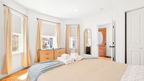Quarto com uma cama grande, cómoda de madeira, espelho e porta.