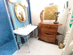 A bathroom with a white sink, a mirror, a wooden vanity, and a wall-mounted sculpture. - SAINT-JEAN DE LUZ, SAINTE-BARBE VILLA 3 PIECES AVEC PISCINE (ST JEAN DE LUZ)