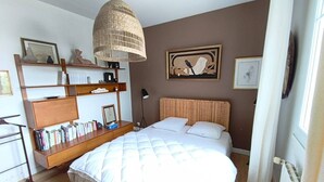 Een slaapkamer met een bed, een boekenkast, een hanglamp en twee ingelijste kunstwerken aan de wand.