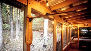 En träveranda med ljusslingor, en trästol och utsikt över ett skogsområde.