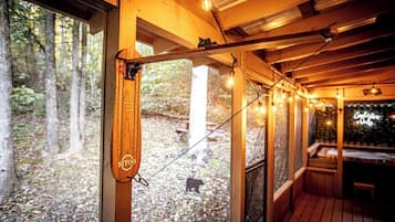 A wooden deck with string lights, a wooden chair, and a view of a forested area.