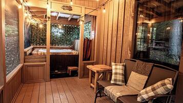 Une terrasse en bois avec un jacuzzi, un banc en bois et un canapé agrémenté de coussins à carreaux.