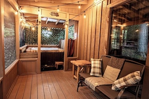Eine Holzterrasse mit Whirlpool, einer Holzbank und einer Couch mit Karokissen.