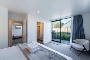 Habitación de hotel moderna con una cama, una silla, un armario y un ventanal corredero a un balcón.