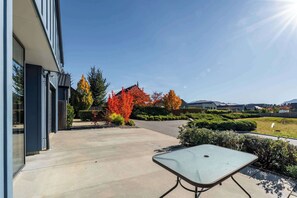 Un edificio moderno con un patio de concreto, una mesa y árboles de colores otoñales.