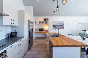 A modern kitchen with white cabinetry, a wooden island, a built-in oven, and a stainless steel refrigerator. - The Snug at Glen Dene (Wānaka)