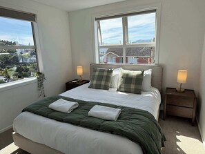 A neatly made bed with a green blanket, two pillows, and two bedside lamps.