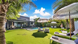 Ein modernes Haus mit Swimmingpool, Sitzgelegenheiten im Freien und einem gepflegten Rasen.