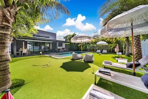 Ein modernes Haus mit Swimmingpool, Sitzgelegenheiten im Freien und einem gepflegten Rasen.