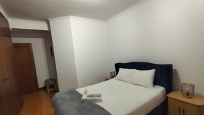 Un dormitorio con una cama, una mesita de noche, un armario de madera y un taburete pequeño.