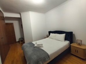 A bedroom with a bed, a nightstand, a wooden wardrobe, and a small stool. - Oceanview First Line with 2 Pools 6 (Ovar)