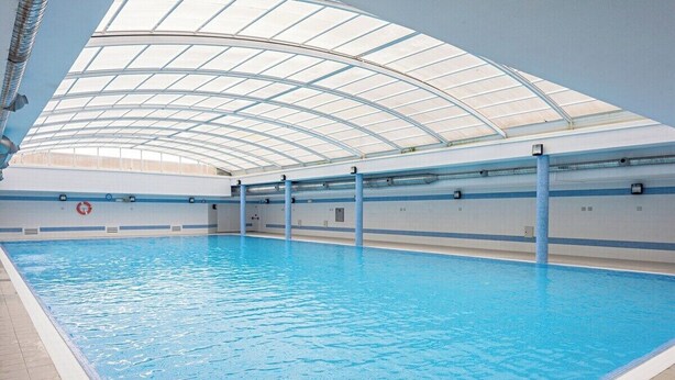 Una piscina interior con techo de cristal curvo, agua cristalina y marcas de seguridad azules.