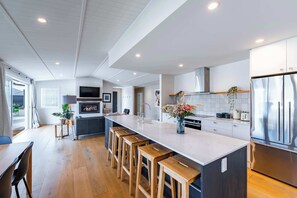 A modern kitchen with a large island, wooden stools, a built-in oven, and stainless steel appliances. - Farrant Drive Hideaway with Mountain Views (Wānaka)