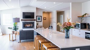 Een moderne keuken met een centraal eiland, houten krukken, een televisie boven de open haard en een magnetron.