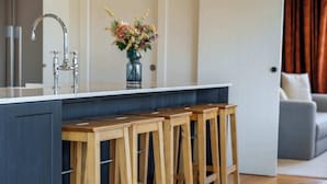 Een keuken met een centraal eiland, houten barkrukken, een roestvrijstalen kraan en een vaas met bloemen.