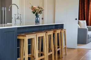 A kitchen with a central island, wooden bar stools, a stainless steel faucet, and a vase with flowers. - Farrant Drive Hideaway with Mountain Views (Wānaka)