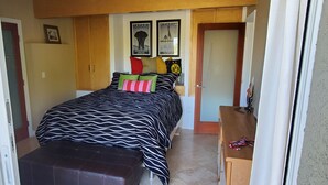 Quarto com uma cama, um guarda-roupa de madeira, uma mesinha e uma porta.
