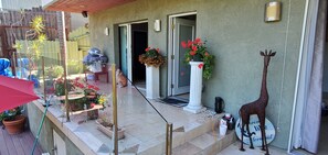 Une terrasse avec un parasol rouge, des plantes en pot, une colonne blanche ornée de fleurs et une statue de girafe.