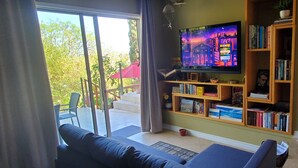 Sala de estar com televisão, estantes de livros, um sofá e vista para o exterior.