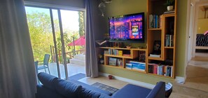 Un salon équipé d’un téléviseur, de bibliothèques, d’un canapé et offrant une vue sur l’extérieur.