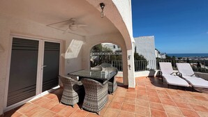 An outdoor patio with a table and chairs, a ceiling fan, and a view of the sea.